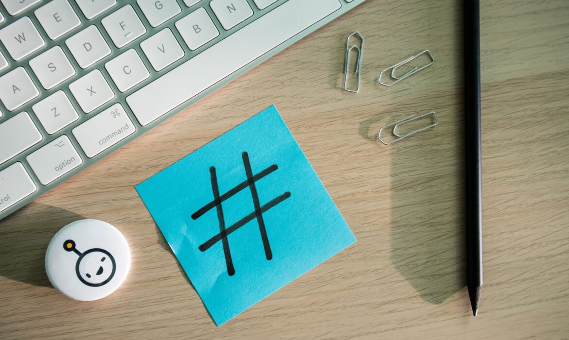 Top view of hashtag symbol on sticky note with keyboard and stationery on desk.