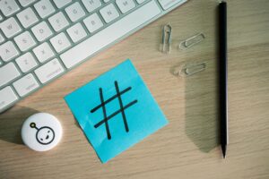 Top view of hashtag symbol on sticky note with keyboard and stationery on desk.