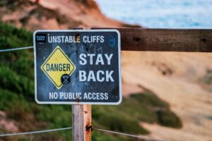 Warning sign indicating danger due to unstable cliffs, advises staying back. Outdoors setting.